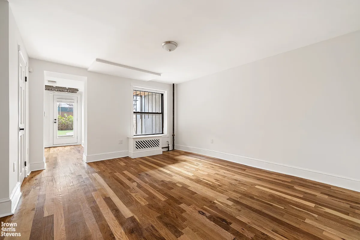 Garden level bedroom with white walls, hardwood floors and backyard access