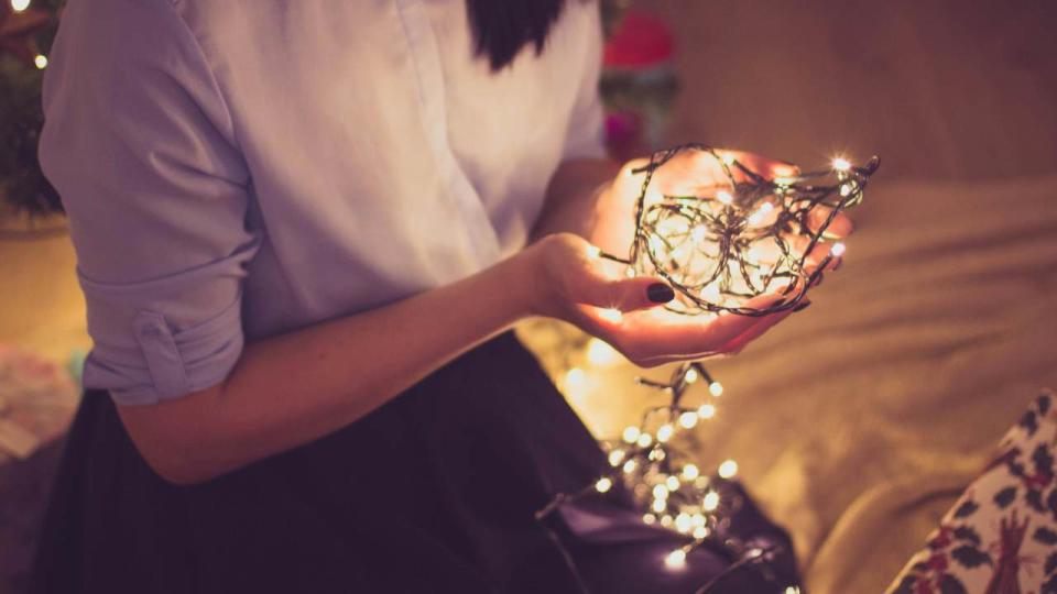     A woman kneels down and holds a bunch of Christmas lights in her hands. 