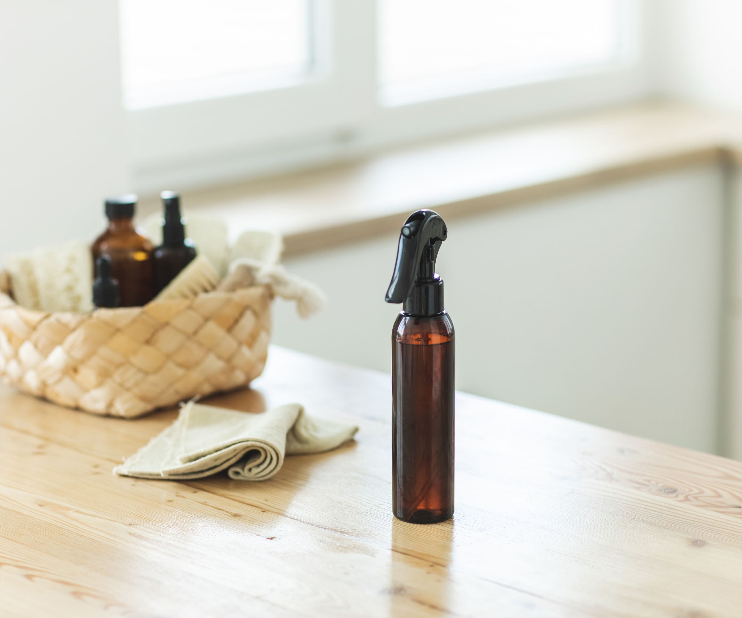 Wooden kitchen counter with a wicker basket full of amber spray bottles, linen clothes and natural looking scrub brushes