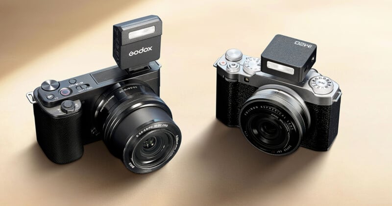 Two digital cameras are shown, each equipped with a mounted external flash. The camera on the left has one "Godox" Flash, while the camera on the right has one "AMED" Flash. Both cameras have an elegant black and silver design.