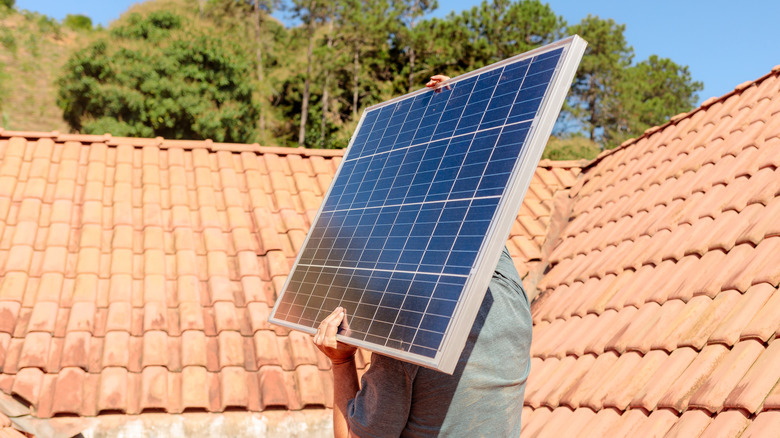 Person carries a solar panel on the top of a roof with red -cut