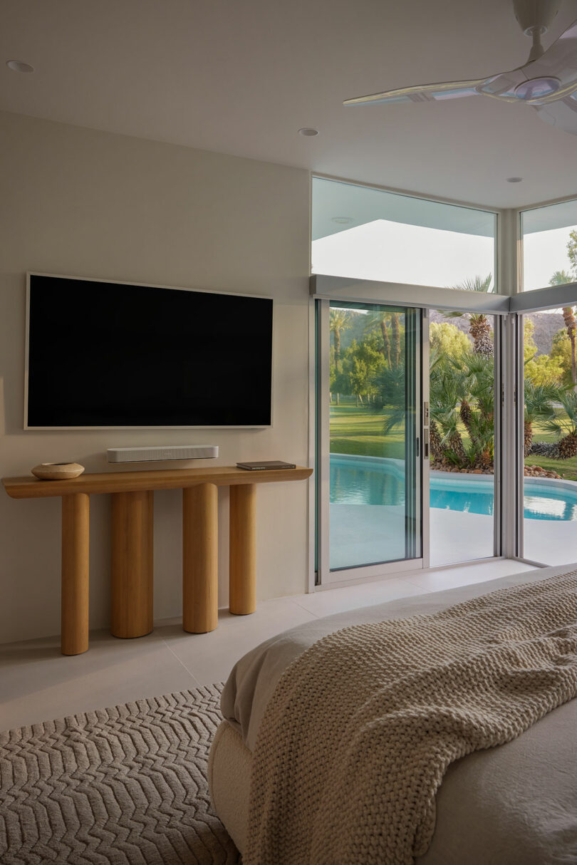 A modern bedroom with a large bed, a wall mounted on a wall and a view of a pool and a garden through sliding doors.