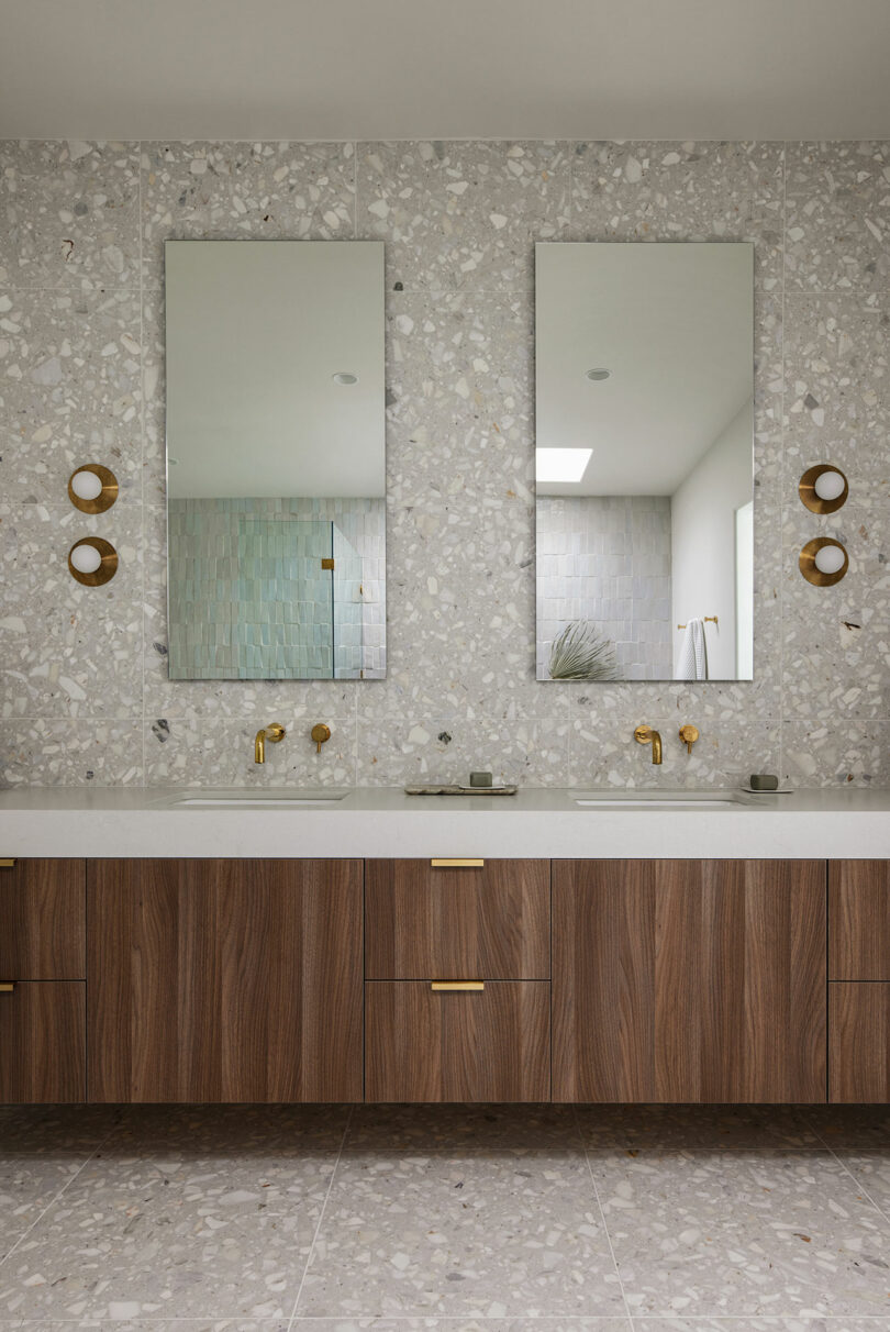 Modern bathroom with large washbasin, dual level, terrazzo walls and brass lights. Light wooden cabins and a tiled shower area are visible.