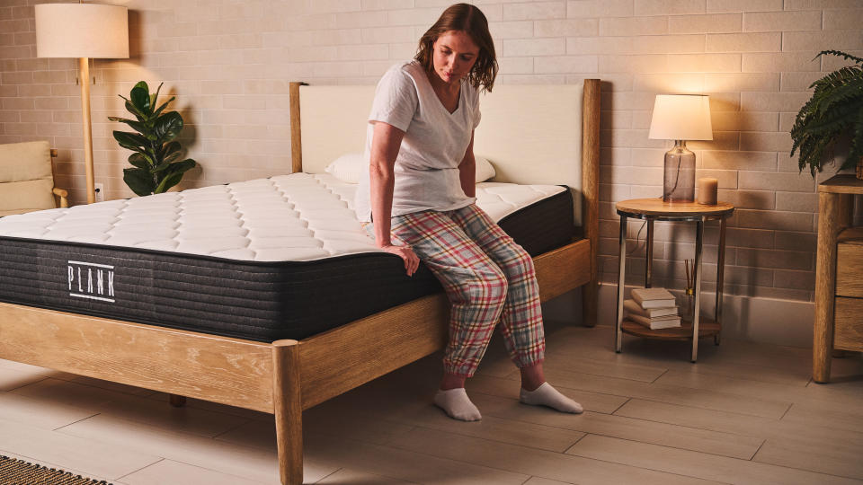 One person sits on the edge of the Plank company mattress, particularly firm to test the edge support