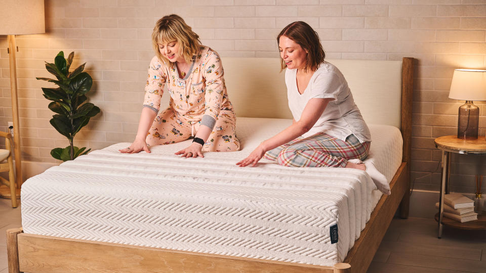     Two women sit on a Leesa legend -Hybrid mattress in a bedroom and test the feeling of the mattress. 