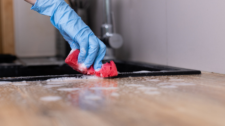 Hand wears blue glove that cleans a worktop with a red sponge