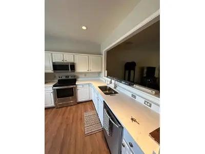 A recently converted cuisine of BNG Remodel with clean white cupboards, stainless steel devices and wooden floors. The open layout and a large pass-through window improve space with natural light and connectivity.