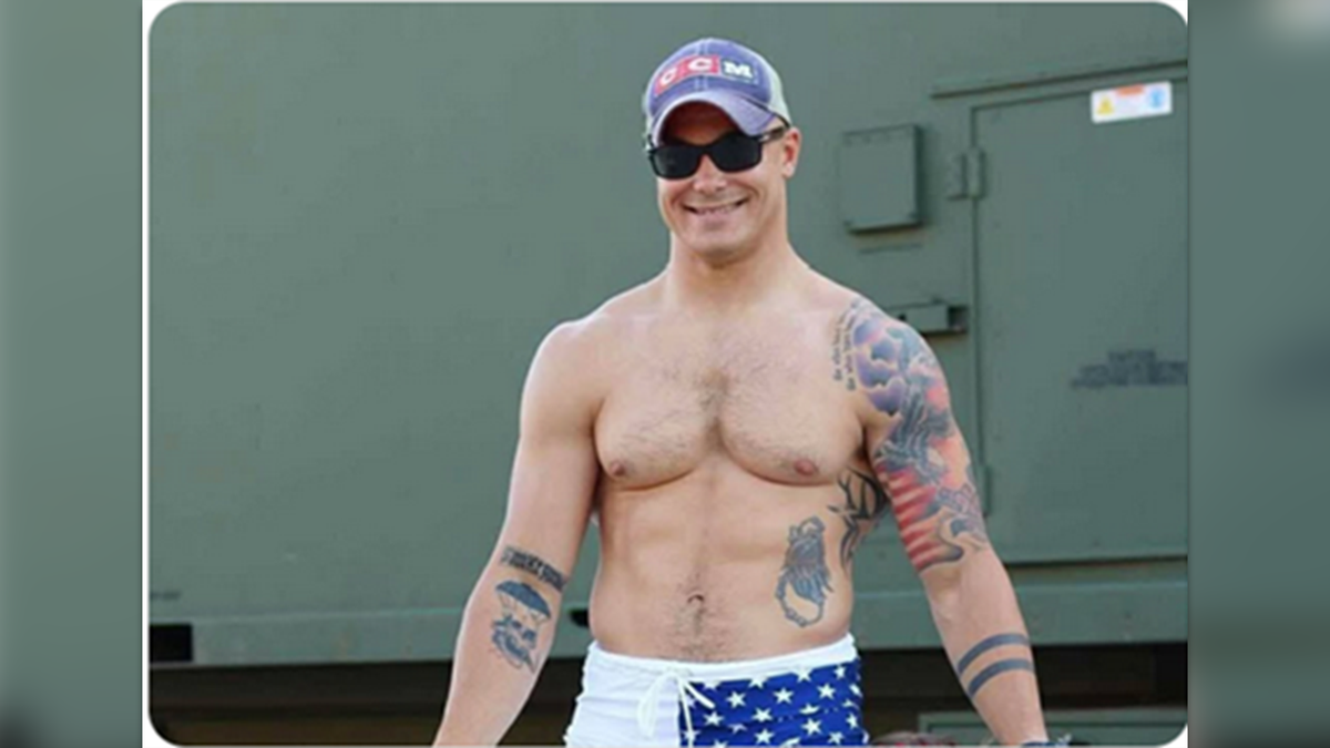 Travis Decker with a clean shave and shirt without a shirt and shows tattoos on both arms and his left side