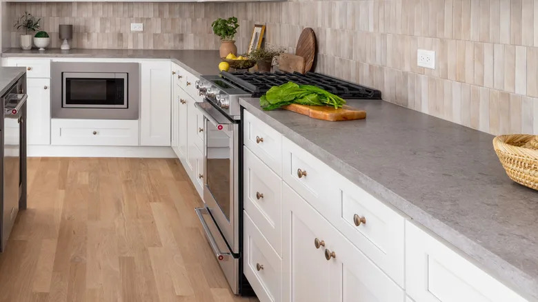 Sand and stone kitchen with gray quartz worktops, white cupboards and a vertical tile back splash.