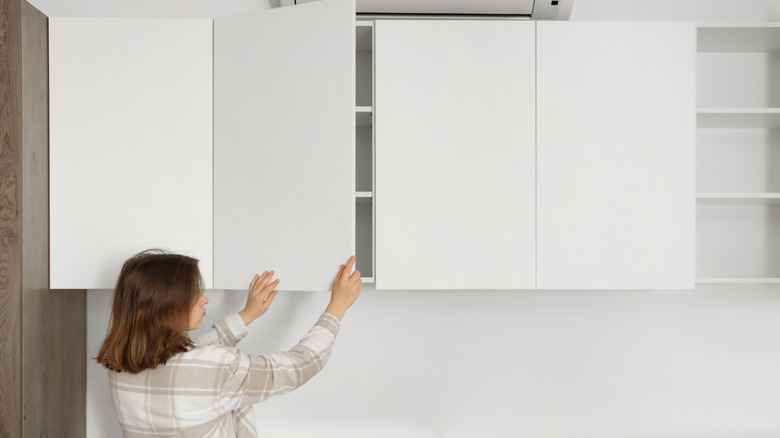 A woman who opens a set of white kitchen cupboards