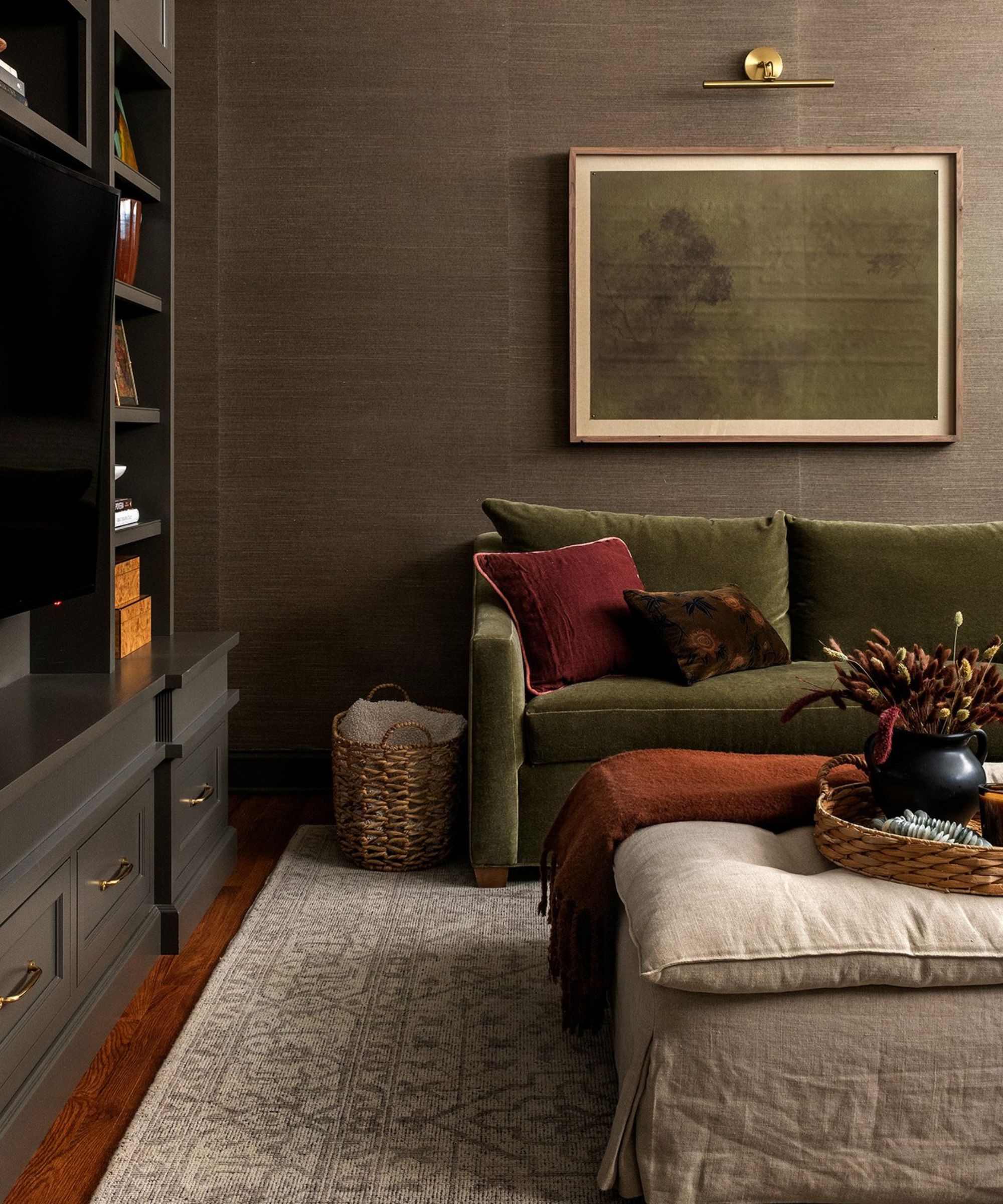Dark living room with patterned carpet, green sofa with pillow, framed minimalist painting, partly black bookshelf left, footsters, wooden floors.