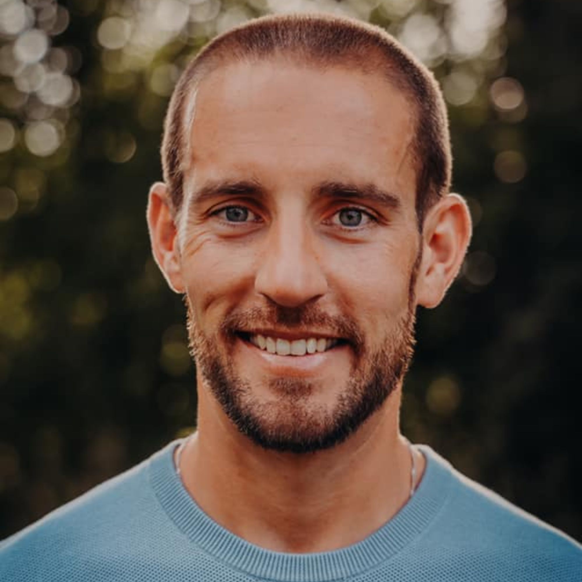 A head shot by Scott Schrader - a man who wears a blue jumper who smiles into the camera