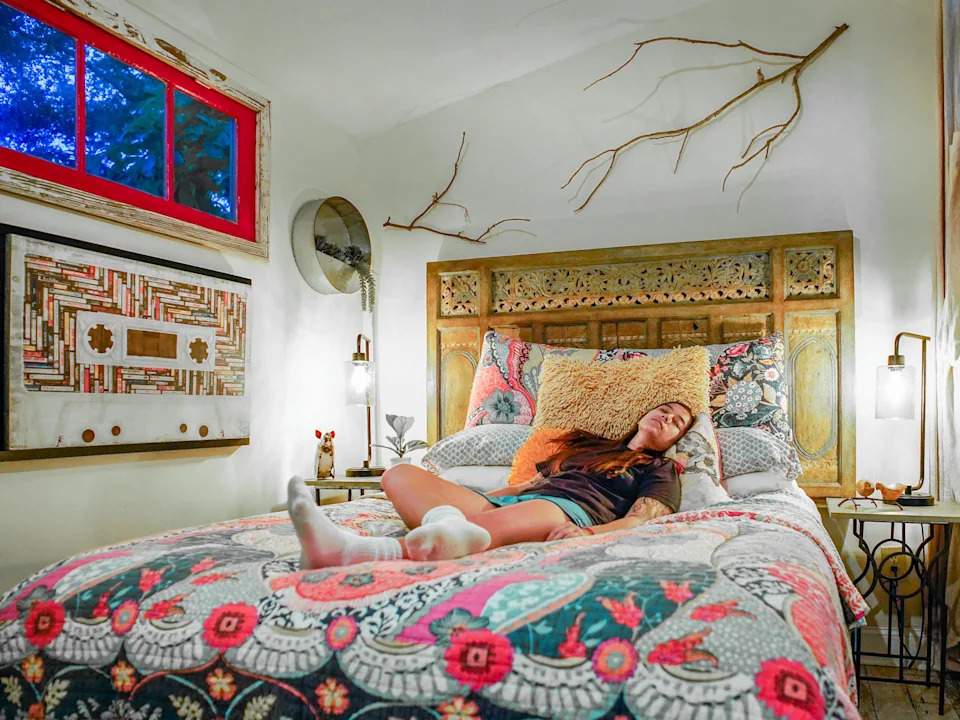 The author rests in a bed with a lively quilt and a decorated headboard
