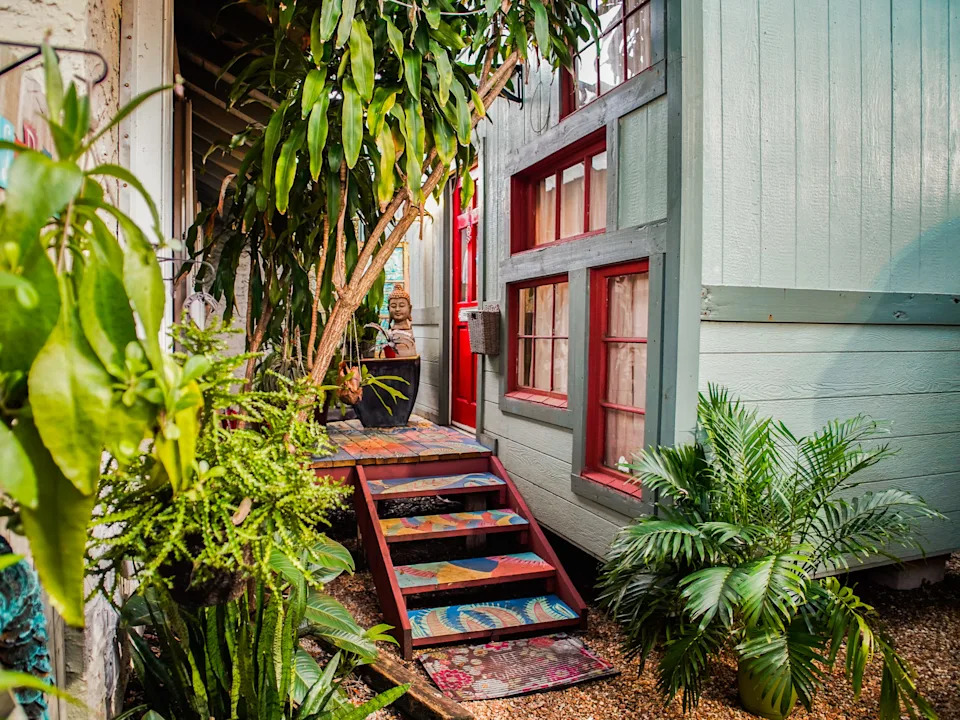 The exterior of a lively tiny home with a painted veranda and trees on the left