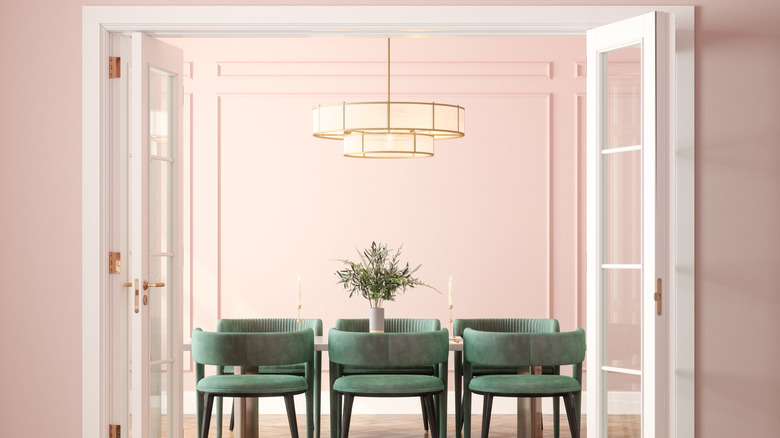 A chandelier hangs above the table in a soft pink dining room