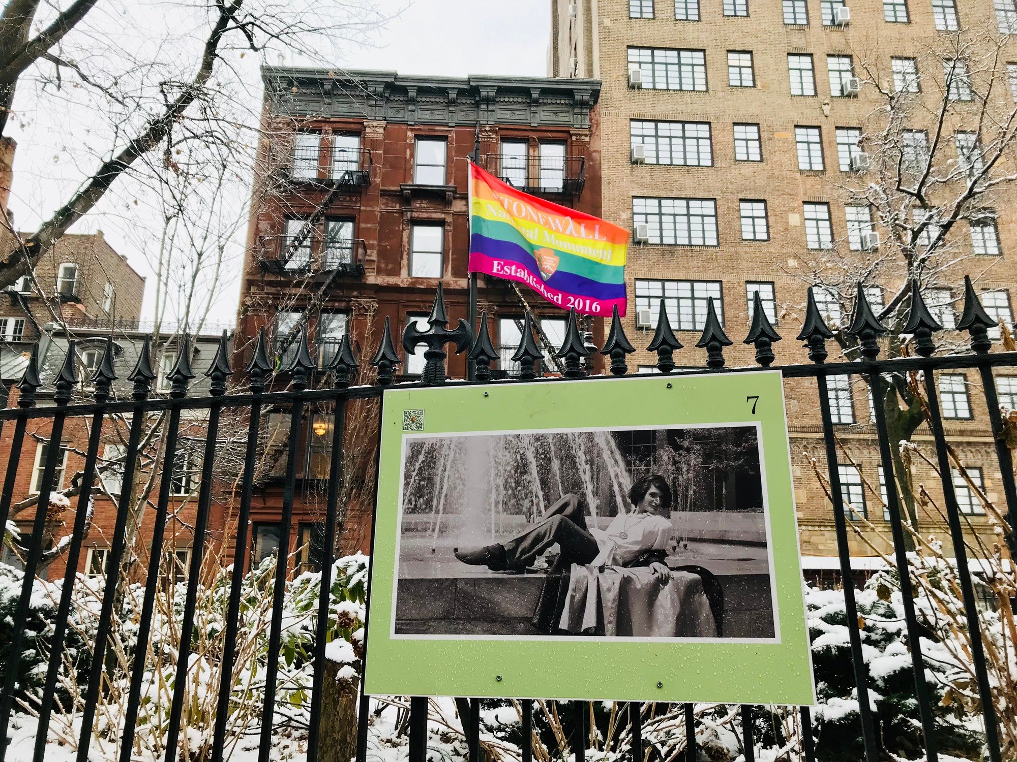 A sign from the Christopher Park fence exhibit with a photo taken by Kay Tobin of Sylvia Rivera lying on a fountain in Ne