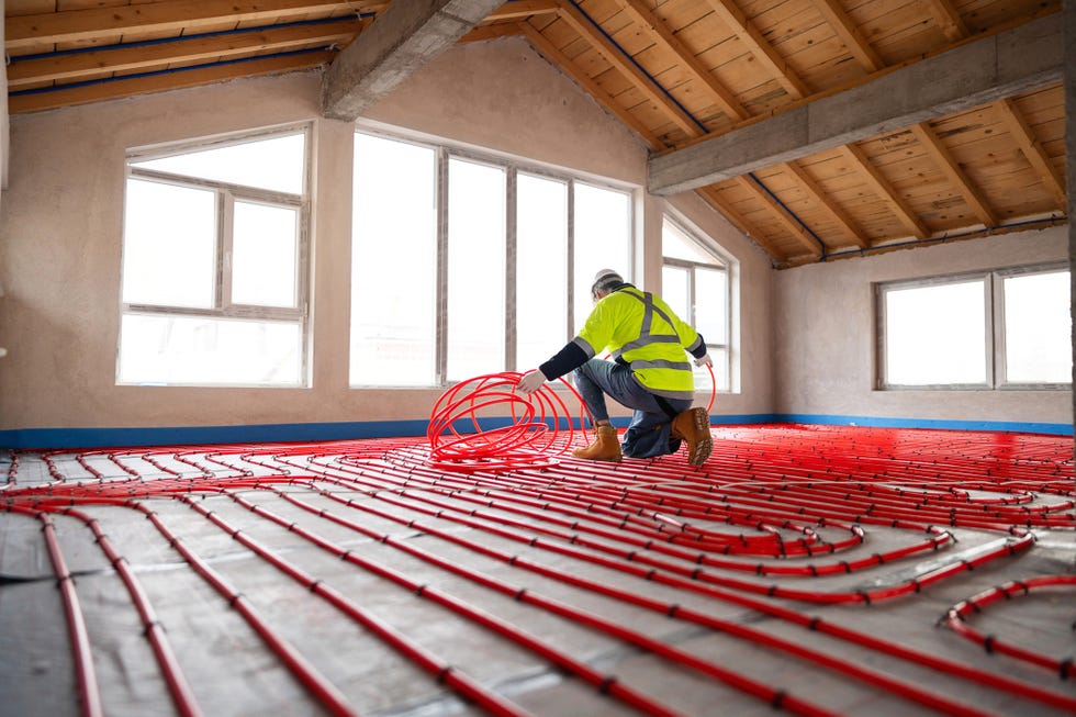 Worker installs red hoses for underfloor heating in a new building